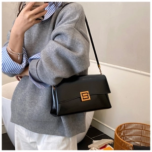 Détail du sac à bandoulière en cuir noir mat avec boucle dorée porté avec un pull en maille
