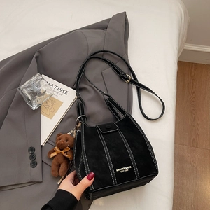 Gros plan du sac cabas noir mat avec des coutures blanches et un charme d'ours brun