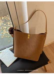 Détail d'un sac seau marron avec fermoir doré, logo et pompon décoratif suspendu