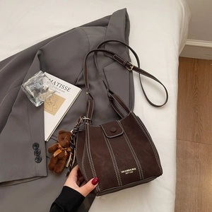 Vue détaillée d'un sac seau marron foncé avec surpiqûres et charm d'ours en peluche