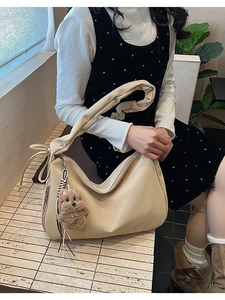 Detail of beige pleated cloud bag with wide shoulder strap and cute bear charm