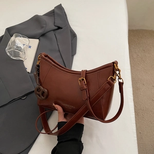 Dettaglio della borsa sottobraccio in pelle marrone scuro con fibbia dorata e ciondolo