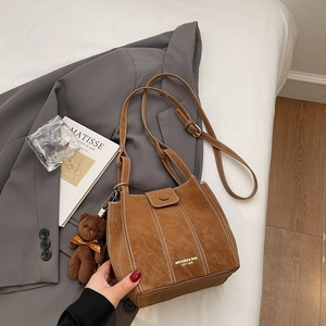 Détail du sac seau en daim marron avec surpiqûres blanches et charme d'ours