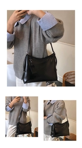 Detail shot of black leather tote bag with adjustable strap and decorative tag in lifestyle setting