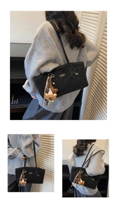 Detail of black tote bag with white contrast stitching, gold logo, and cute bear charm