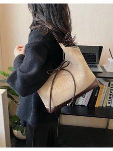 Detail of a large beige and brown tote bag with ribbon bow and embossed letters