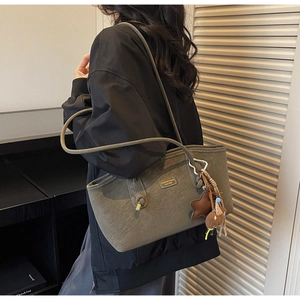 Olive green tote bag with plush bear charm and fashion label shown on model shoulder