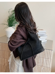 Makroaufnahme von Prägebuchstaben und Kordelschleife an der schwarzen Wildleder-Schultertasche