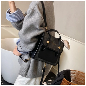 Détail du sac à dos en daim gris avec rabat noir, boucle dorée et pompon décoratif doux