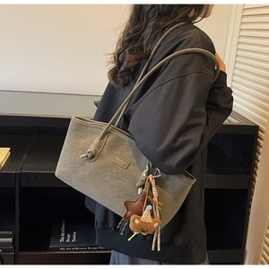 Detail of olive green tote bag with plush bear charm and thin shoulder straps on model