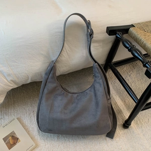 Détail du sac hobo en daim gris avec bandoulière réglable sur un fond de lit confortable