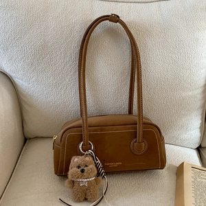 Detail of brown faux suede handbag with plush bear charm on a soft textured sofa