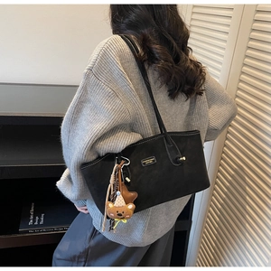 Detail of black tote bag with teddy bear charm and fashion leather patch on shoulder