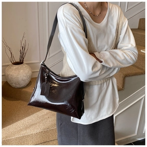 Detail of a dark brown glossy leather tote bag showing a side profile and texture