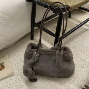 Dettaglio borsa a secchiello in peluche grigio con tracolla in pelle marrone su tappeto
