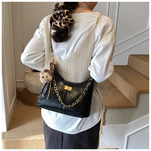 Detail of black faux leather hobo bag with gold chain and plush bear charm on model