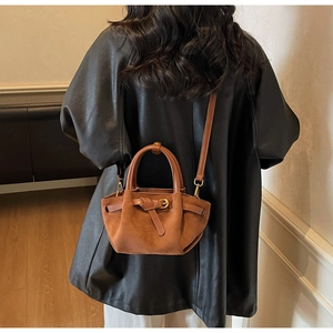 Borsa a mano in camoscio marrone con fibbia indossata da modella in ambiente chic
