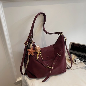Detail of burgundy tote bag featuring decorative straps and star plush charms on desk