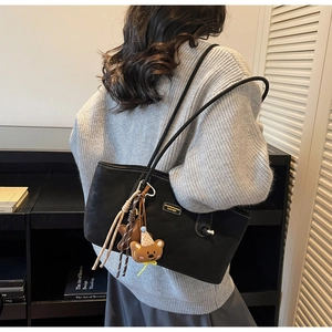 Close-up of black leather tote bag with brown bear charm and tassel detail on a strap