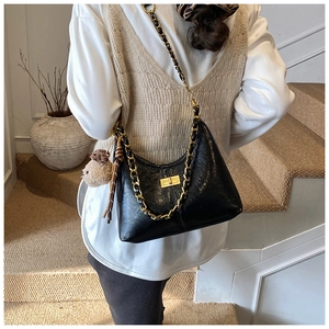 Detail of black glossy dumpling bag with gold chain strap and plush puppy charm