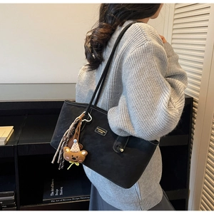 Detail of black matte leather tote bag with plush bear charm and woven tassel accent