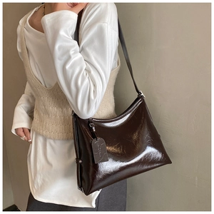 Shoulder shot of a glossy chocolate brown patent leather tote bag with vintage texture