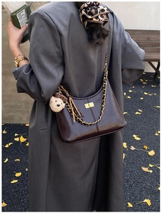 Detail of dark brown glossy leather bag with gold chain strap and cute bear charm