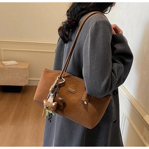 Detail of brown faux suede tote bag with plush bear charm and metallic logo plaque