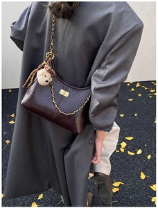 Detail of dark brown leather crossbody bag with gold metal lock and plush bear pendant