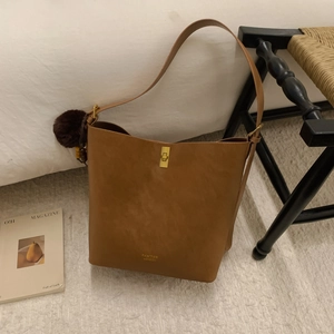Détail d'un sac seau en cuir marron avec fermoir doré et accessoire de boule en peluche