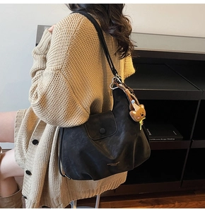 Detailansicht der schwarzen Ledertasche mit Plissee-Design und braunem Bärenanhänger