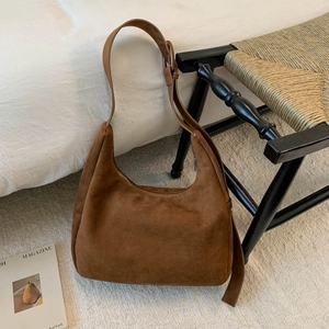 Détail d'un sac hobo en daim marron avec boucle argentée réglable sur un tapis élégant clair