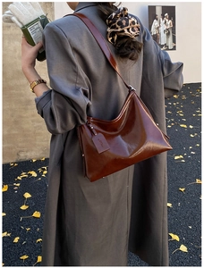 Detail view of glossy dark brown tote bag worn with grey coat in autumn scenery