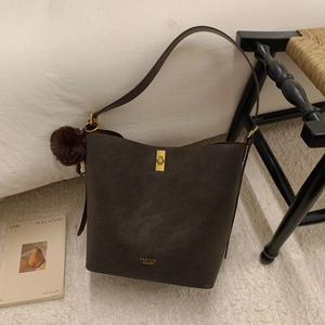 Détail du sac seau vintage mat avec fermoir rotatif doré et pompon en peluche marron