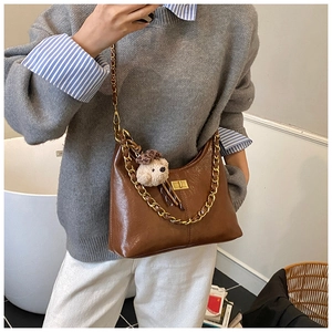 Close-up of brown faux leather bag featuring a gold chain and plush bear charm