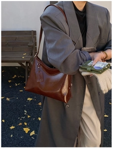 Close-up of a dark brown oil-wax leather tote bag carried by a model in autumn street style
