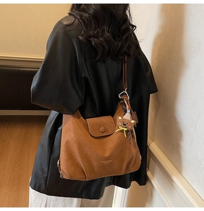 Detailansicht der karamellbraunen Ledertasche mit Bär-Anhänger und modischer Beschriftung