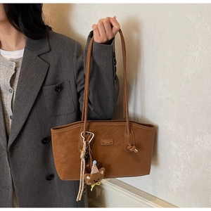 Detail of a brown leather tote bag with a cute plush bear pendant and fashion brand tag