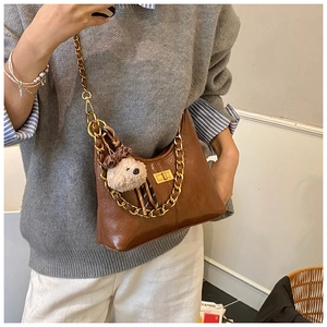 Detailed shot of brown crescent bag with gold chain and plush bear charm accent