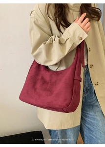 Gros plan du sac hobo en daim bordeaux porté par un mannequin au style rétro épuré