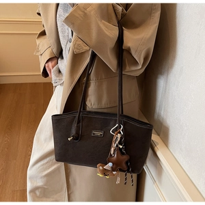 Detail of dark brown leather tote with white contrast stitching and charm accessories