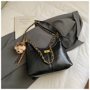 Detail of black leather dumpling bag featuring gold chain strap and teddy bear charm
