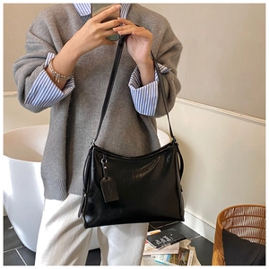 Detailed view of black glossy tote bag with minimalist shoulder strap and leather tag