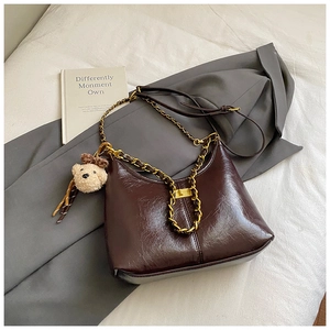 Detail shot of a dark brown crescent bag with a chunky metal chain and plush bear charm