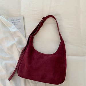 Détail du sac hobo en daim bordeaux sur tissu blanc avec des accessoires décoratifs