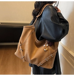 Macro detail of brown leather tote bag showing fine matte texture and side buckle design