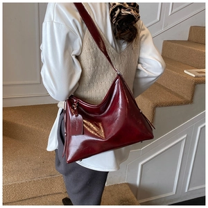 Close-up of a burgundy patent leather hobo shoulder bag worn by a model in soft indoor light
