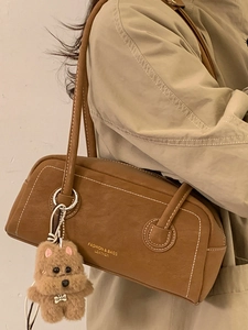 Brown suede crossbody bag with plush dog charm worn by a model in a beige coat