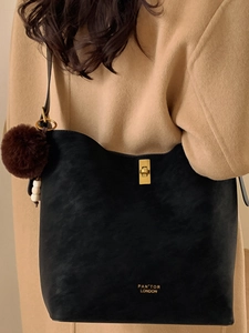 Sac seau rétro noir mat avec boucle dorée et breloque pompon porté par un mannequin