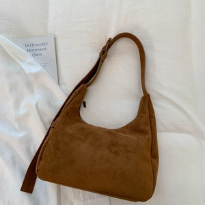 Gros plan d'un sac hobo en daim marron avec bandoulière sur un fond de tissu blanc minimaliste
